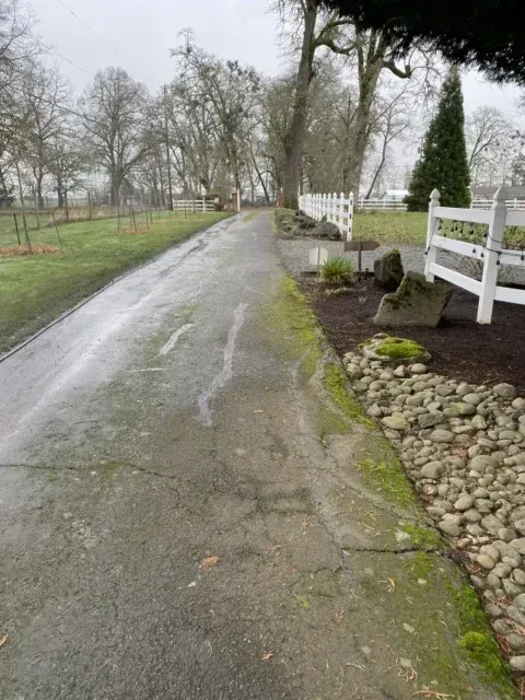 Wet country lane beside white fence and stone landscaping on a cloudy day