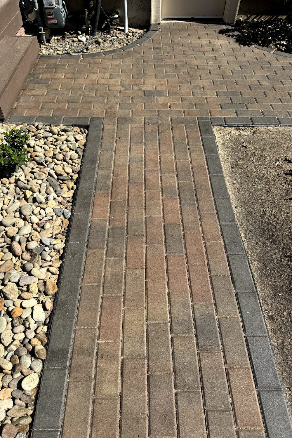 Brick walkway bordered by rocks and mulch leading to a patio area