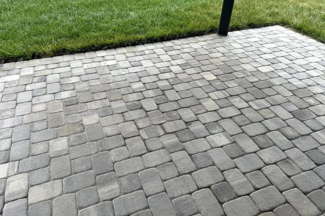 Gray stone paver patio beside a strip of green grass with a black post.