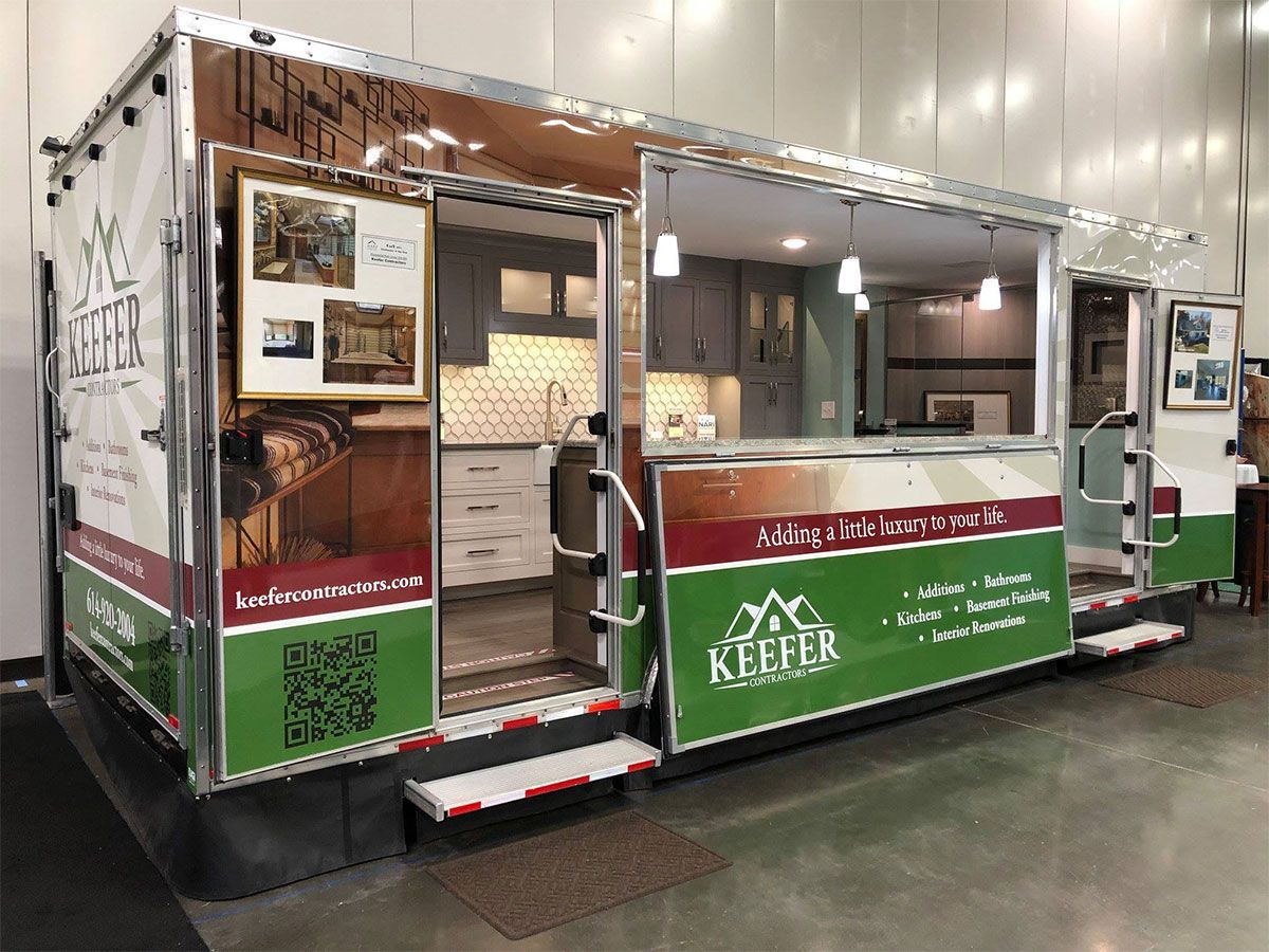 Green portable concession trailer with open serving window and red-white trim inside a warehouse.