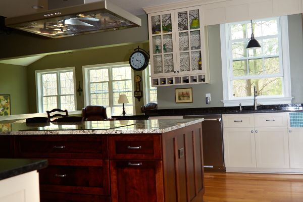 Bright kitchen with wood island, white cabinets, large windows, and a hanging clock