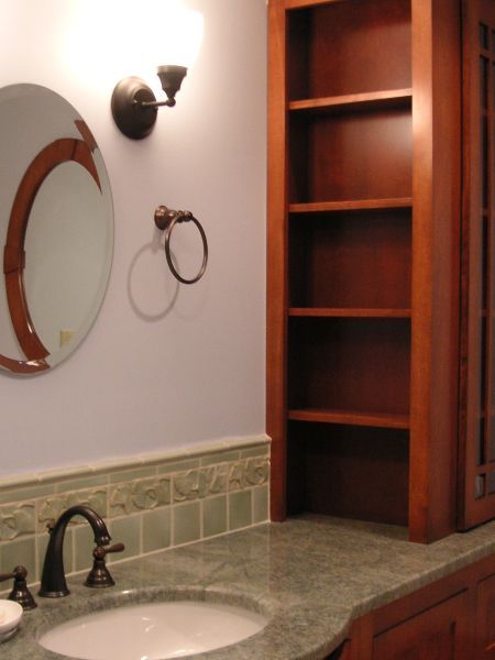 Bathroom vanity with round mirror, wall sconce, sink, and built-in wooden shelves.