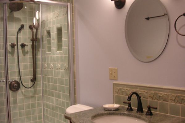 Bathroom with glass shower, granite sink, and round mirror on a light purple wall