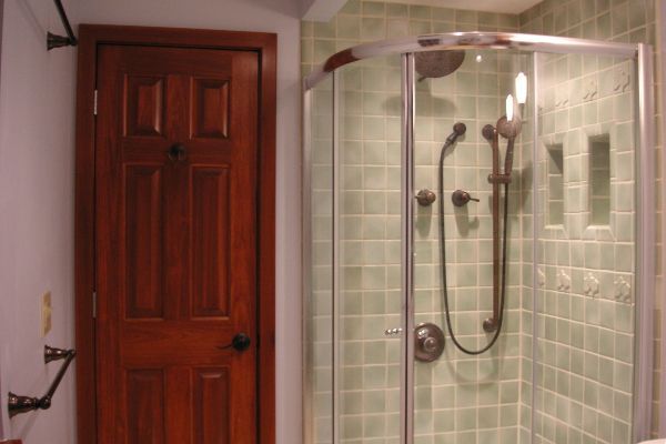 Bathroom with a wooden door and a glass-enclosed shower with pale green tile walls