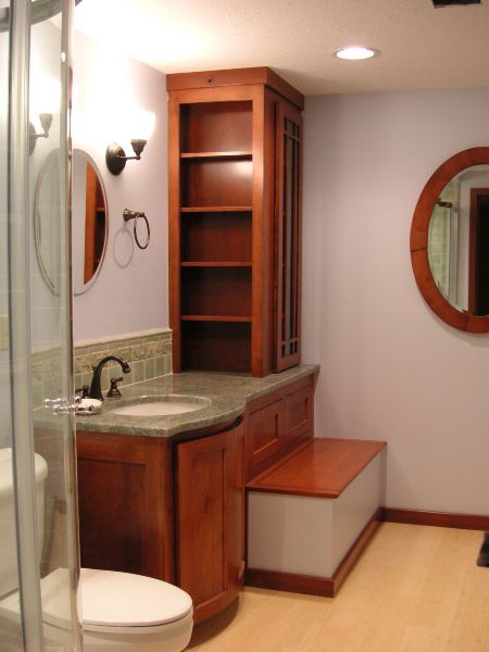 Compact bathroom with wooden vanity, sink, round mirror, shower, and built-in storage bench.