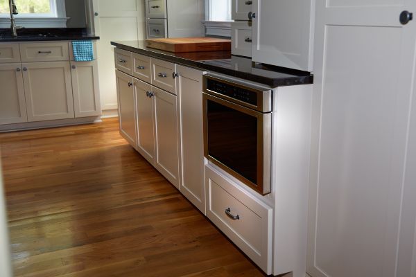 Bright kitchen with white cabinets, black countertops, hardwood floor, and stainless steel oven.