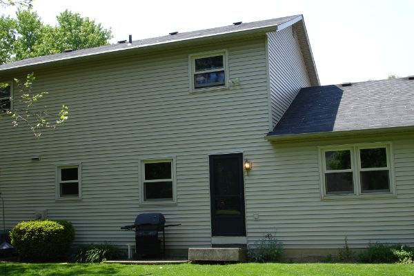 Two-story beige house with a dark green door, white trim, and a small lawn in front.