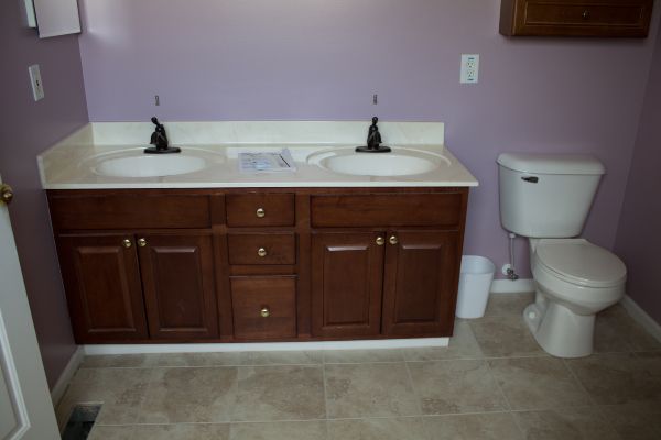 Bathroom with double vanity, brown cabinets, white countertop, and toilet against a purple wall.