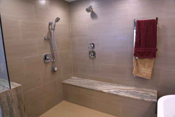 Accessible shower with bench, grab bars, handheld showerhead, and red towel on tiled wall