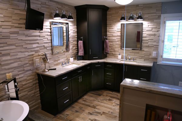 Modern bathroom with dark cabinets, double vanity, mirrors, wall sconces, and tiled walls