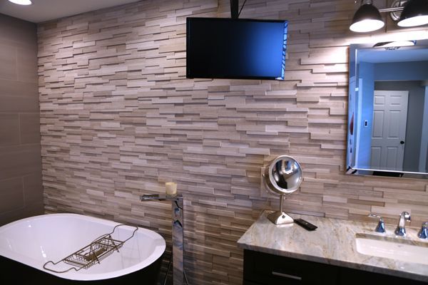 Modern bathroom with stone-tile wall, wall-mounted TV, bathtub, and vanity sink.