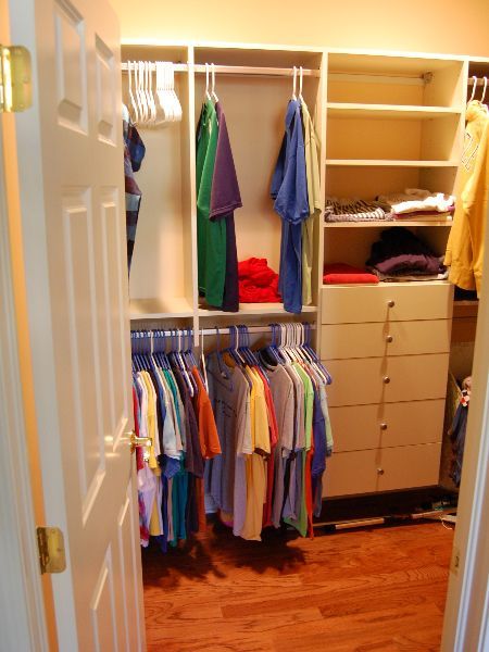 Open closet with hanging clothes, drawers, shelves, and hardwood floor in a bedroom.