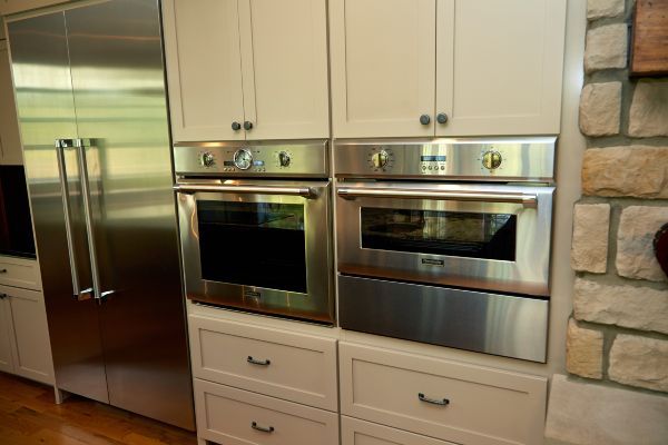Kitchen with stainless steel refrigerator and built-in oven and microwave beside stone wall cabinets