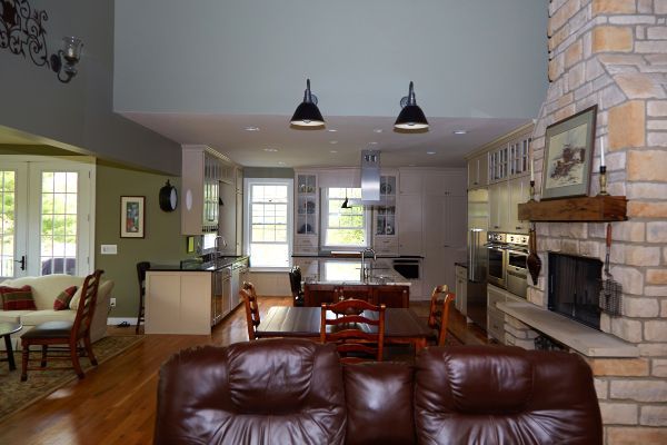 Open-plan living room and kitchen with leather sofa, dining table, pendant lights, and stone fireplace