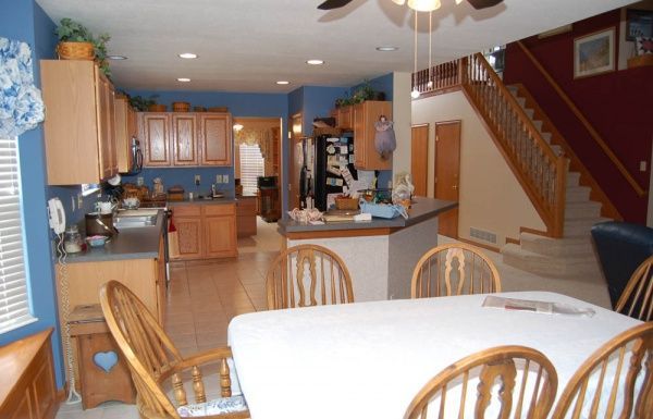 Kitchen and dining area with wooden table and chairs, blue walls, cabinets, and staircase in the background