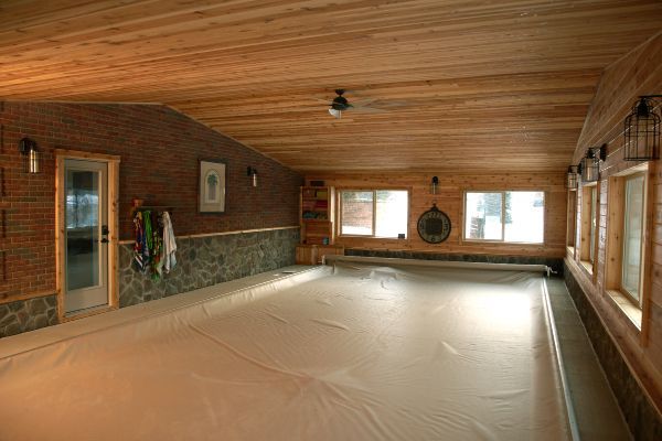 Empty indoor pool room with wood-paneled ceiling, brick walls, and covered pool floor
