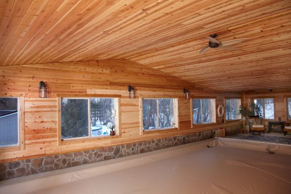 Wood-paneled screened porch with windows, stone base, and empty floor space