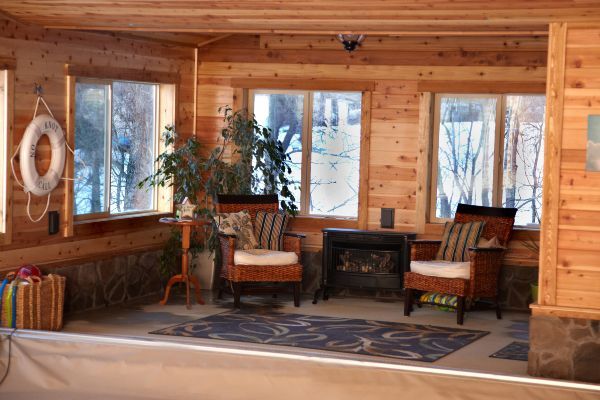 Cozy log cabin living room with large windows, two armchairs, a wood stove, and a patterned rug.