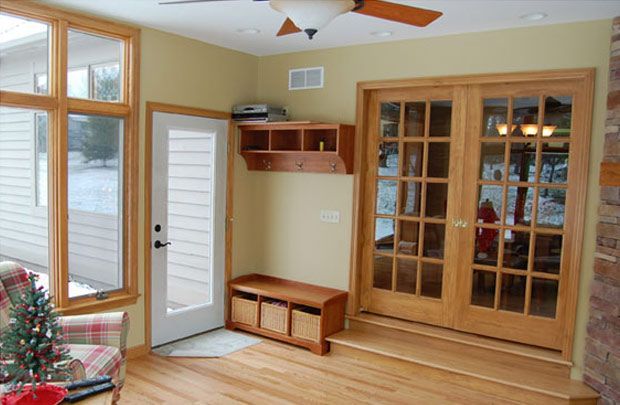 Sunlit living room with wood floors, French doors, bench, and windows by a small Christmas tree