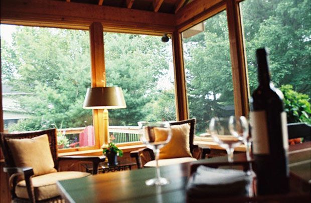 Cozy cabin dining area with wooden beams, large windows, lake view, and a wine bottle on the table