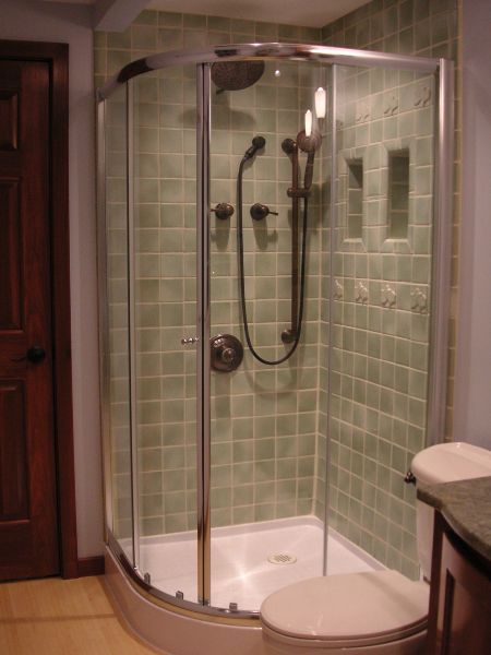 Corner glass shower enclosure with green tile walls and a white shower base and seat