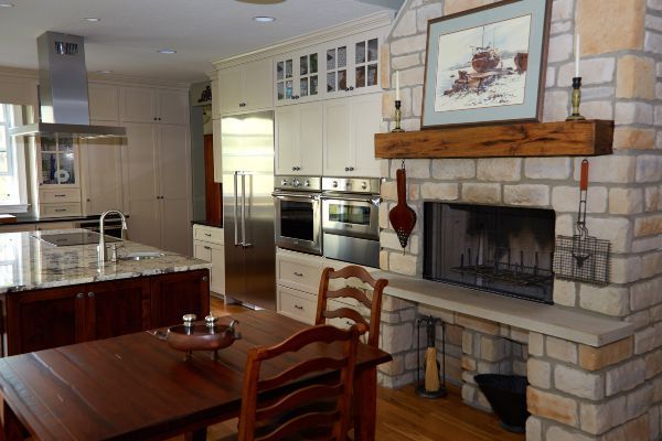 Bright kitchen and dining area with stone fireplace, stainless appliances, and wooden table