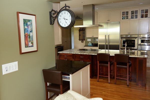 Modern kitchen with dark wood chairs, stainless steel appliances, and a wall clock over a breakfast bar.