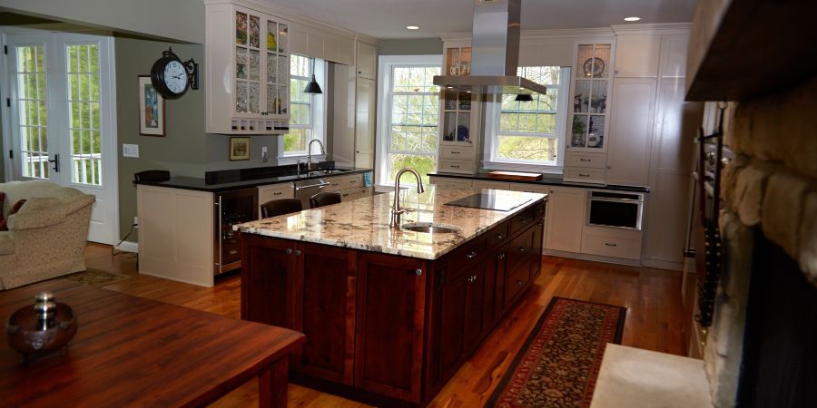 Bright kitchen with a large dark wood island, white cabinets, and a view into another room