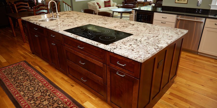 Kitchen island with granite countertop and built-in cooktop on hardwood floor in a warm-toned kitchen