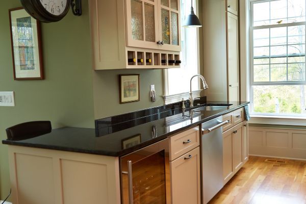 Bright kitchen with beige cabinets, black countertops, and a large window over a wooden floor.