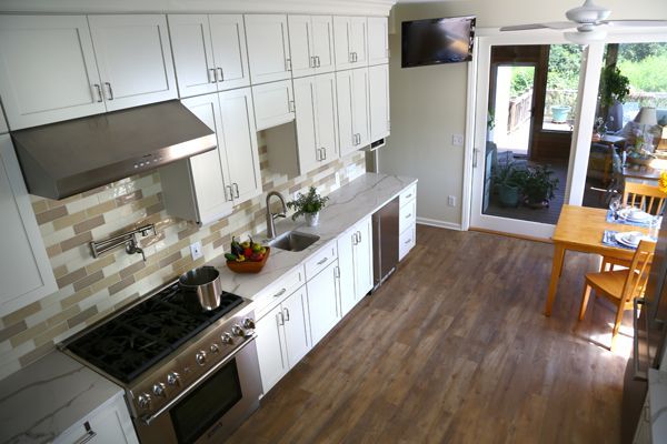 Bright white kitchen with stainless steel stove, wooden floor, and sliding glass door to a patio