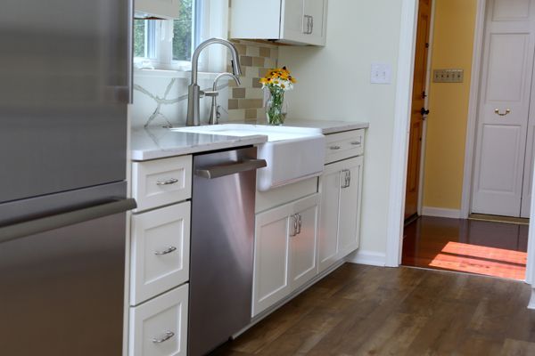 Modern kitchen with white cabinets, stainless dishwasher, wood floor, and a sunlit doorway