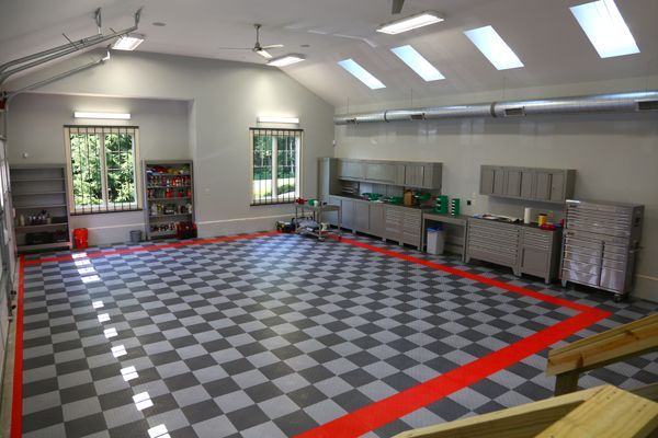 Empty garage with gray checkered floor, red boundary tape, windows, and shelves along the walls
