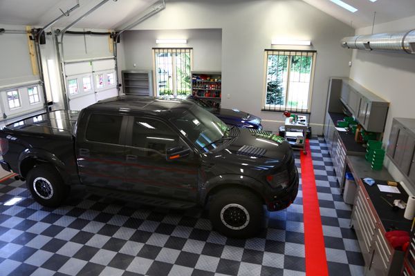 Black pickup truck in a clean garage with checkered floor, windows, and tool cabinets
