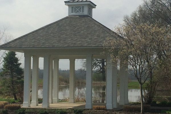 White gazebo with columns by a lake, surrounded by trees in a park