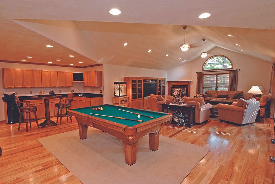 Spacious game room with a pool table, bar stools, couches, and hardwood floors under recessed lighting