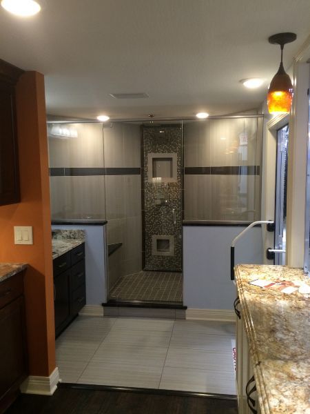 Modern kitchen with tiled floor, dark cabinets, and a walk-in shower visible in the back wall.