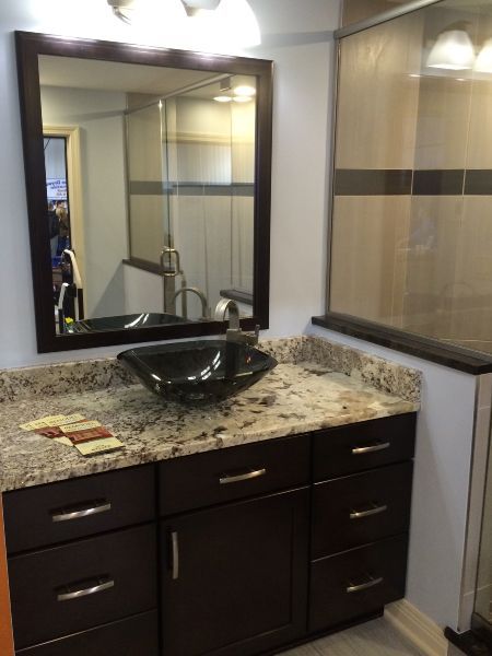 Bathroom vanity with dark wood cabinets, granite countertop, vessel sink, and large mirror, lit by wall sconces