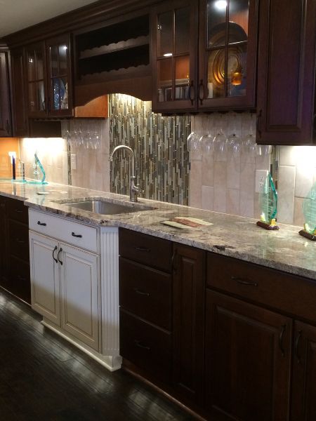 Dark wood kitchen with white cabinets, marble countertop, under-cabinet lighting, and glass tile backsplash