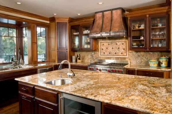 Warm kitchen with large granite island, wood cabinets, copper hood, and stainless steel appliances.