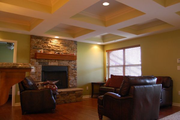 Cozy living room with leather chairs, stone fireplace, and warm yellow walls under a tray ceiling