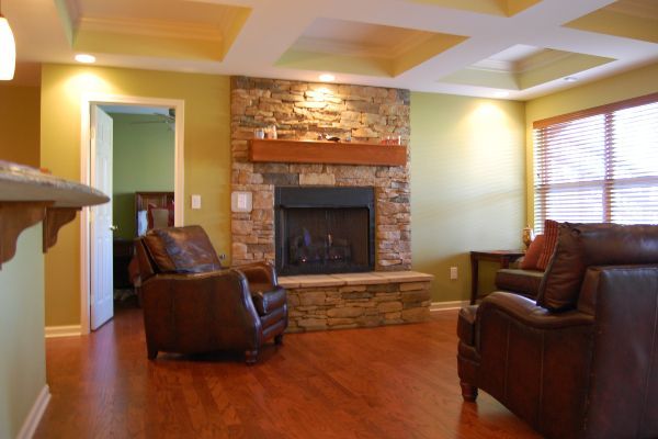 Living room with brick fireplace, leather chairs, wood floors, and window blinds