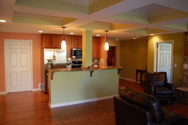 Open-plan living room with hardwood floors, green breakfast bar, kitchen, and dark leather chairs