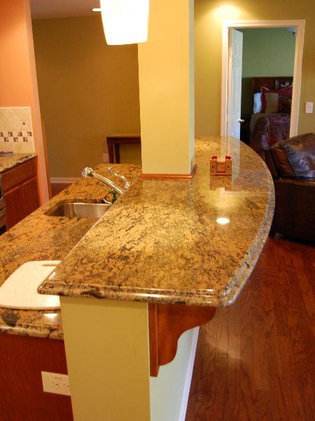 Kitchen with granite island countertop, white cabinets, and warm wood flooring, viewed from the living area