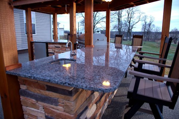 Outdoor patio with granite bar counter, wooden chairs, and a covered stone fireplace at sunset