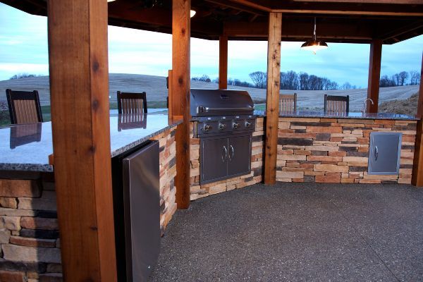 Covered outdoor patio with built-in grill, stone bar, and snowy landscape beyond the railing