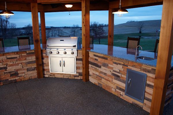 Covered outdoor patio with a built-in grill, brick half-walls, and views of the open landscape.