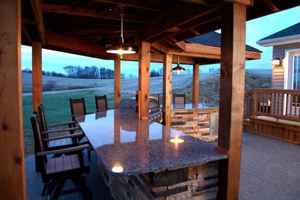 Covered patio with granite bar, wooden chairs, and sunset view over open fields