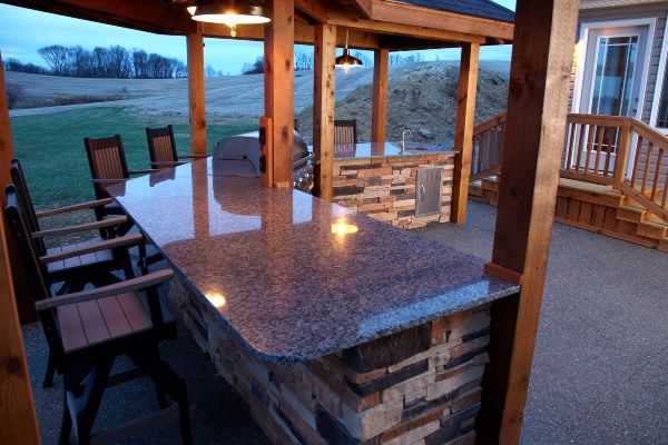 Outdoor granite patio bar with wooden pergola and stone base at dusk
