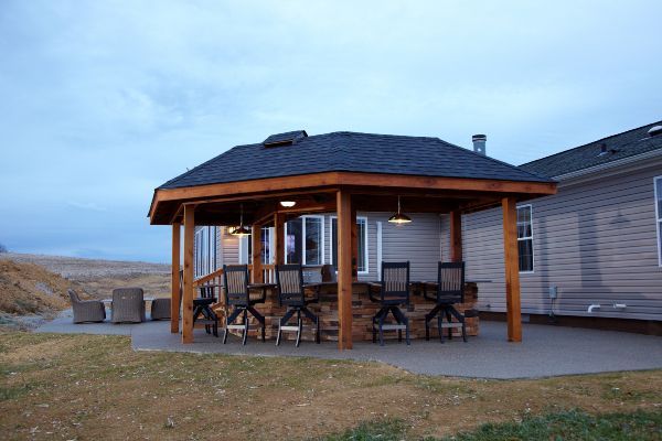 Wooden gazebo with outdoor tables and chairs beside a beach house at dusk